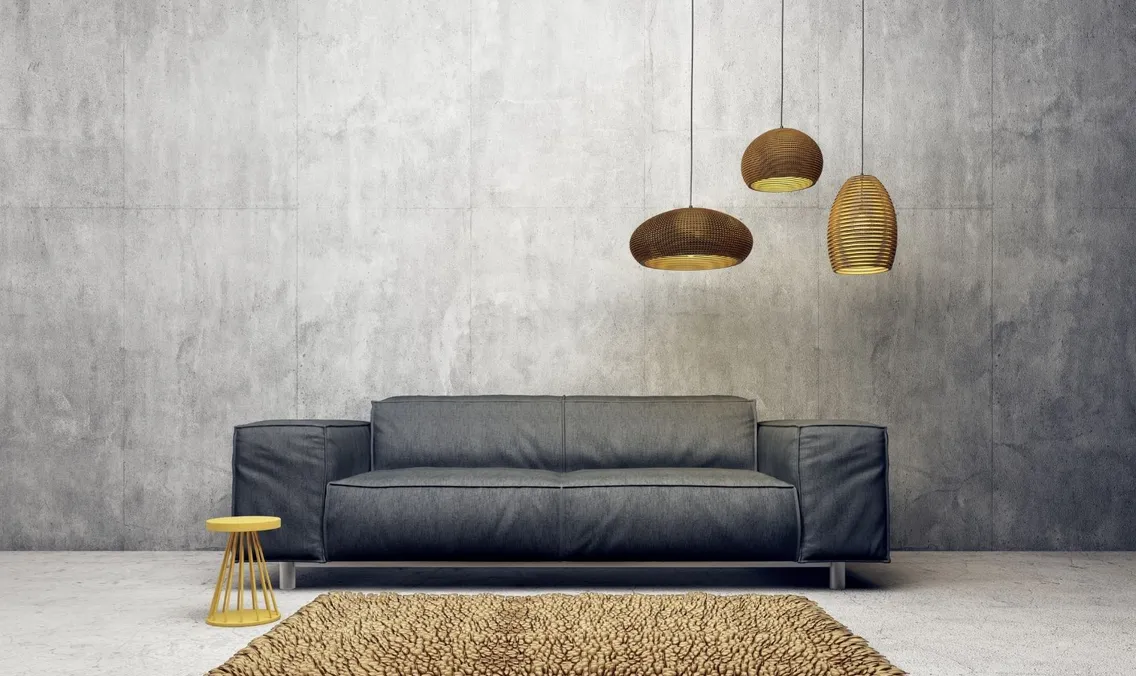 Ciemnoszara sofa przy betonowej ścianie pod trzema lampami wiszącymi